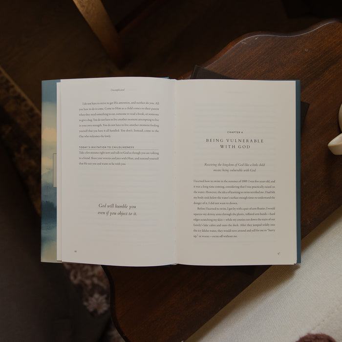 An open book lying on a dark wooden table, showing printed text pages with a light blue-gray cover visible on the left side.