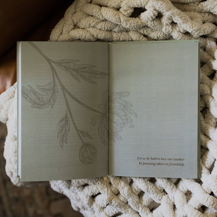 What a friend we have in Jesus opened to a devotional page on a white knitted blanket on a leather couch